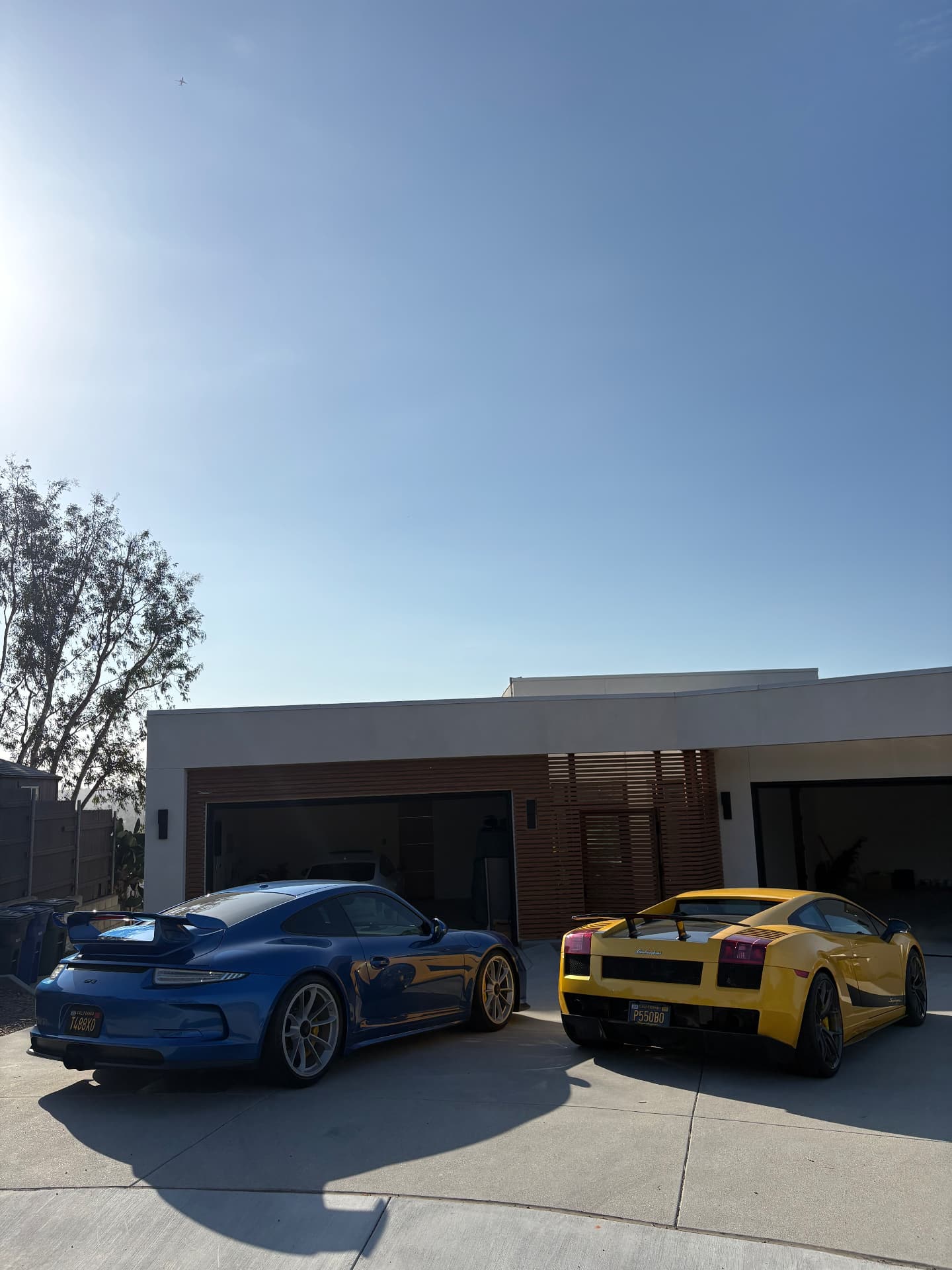 Blue Porsche 911 and yellow Lamborghini parked outside a modern home